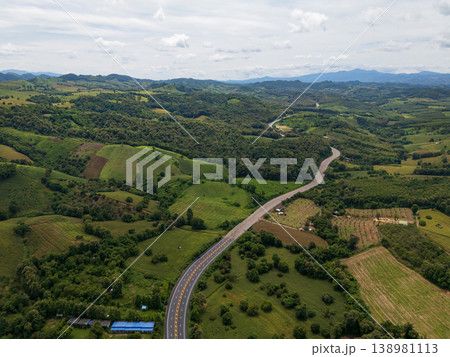 Aerial drone view of Highway winding through lush green mountains between Nan, Thailand. A scenic landscape of the road surrounded by tropical forest and a peaceful countryside Aerial drone view of Highway winding through lush green mountains between Nan, Thailand. A scenic landscape of the road surrounded by tropical forest and a peaceful countryside 138981113