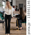 Young businesswoman on a phone call stands at a conference table while colleague seated beside her takes notes on a laptop and notebook during a focused office meeting 138981146