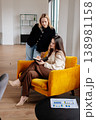 Two businesswomen discussing new project ideas, one writing notes in a planner while the other stands over, engaging in a productive teamwork session in a contemporary office space 138981158