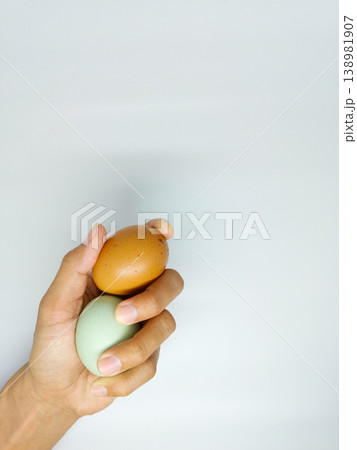 A male hand holding fresh chicken and duck eggs, one brown and one light green, against a plain white background. Focus on smooth shell texture and poultry farming theme A male hand holding fresh chicken and duck eggs, one brown and one light green, against a plain white background. Focus on smooth shell texture and poultry farming theme 138981907