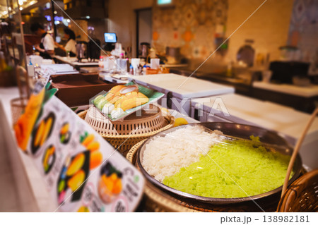 Thai food at the food court in Thailand - cooking and serving the popular Thai dessert mango with sticky rice in Thai Khao Niao Mamuang. Rice sticks: In a large container, two varieties of rice are 138982181