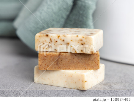 Brown and beige handmade solid soap bars near light green bath towel. Exfoliating scrub soap set 138984493