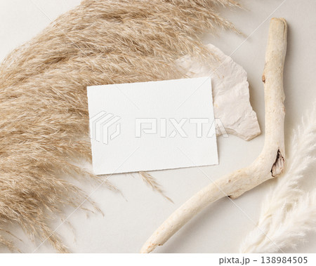 Blank card mockup on beige stone with driftwood and pampas grass top view, boho wedding stationery 138984505