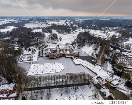 Wide aerial view of Anholt Castle in winter. The moated palace, baroque gardens, and vast parkland are blanketed in snow and ice under a dramatic sky in North Rhine-Westphalia, Germany. 138984554