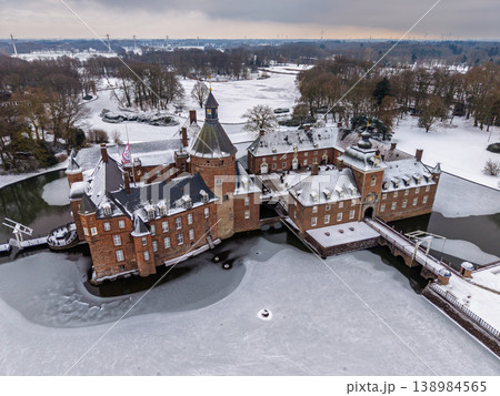 Aerial view of the majestic Anholt Castle in winter. This historic moated palace in Germany is surrounded by a frozen lake and snow-covered park, showcasing stunning red-brick architecture and ice. 138984565