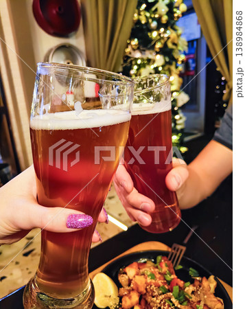 Friends Clinking Glasses of Craft Beer at Cozy Christmas Dinner with Festive Lights 138984868