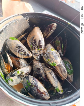 Steamed mussels in creamy garlic sauce with pesto and herbs in a black bowl. Steamed mussels in creamy garlic sauce with pesto and herbs in a black bowl. 138984878