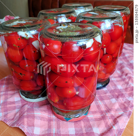 Jars of home-canned red tomatoes with garlic and spices on a checkered towel Jars of home-canned red tomatoes with garlic and spices on a checkered towel 138984879