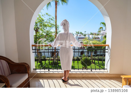 A female tourist on the balcony of her hotel room, wearing a white robe and a towel on her head A female tourist on the balcony of her hotel room, wearing a white robe and a towel on her head 138985108
