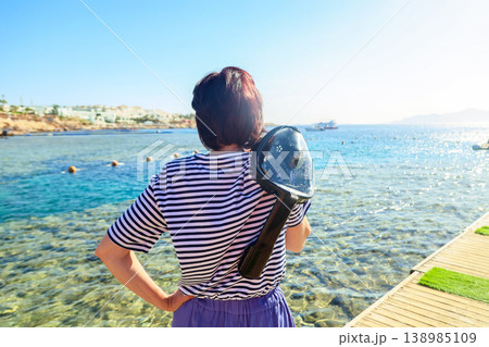 A woman with a diving mask on her shoulder looks at the sea 138985109