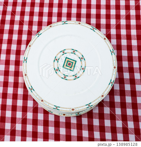Stack of pristine, beautiful plates arranged on a checkered tablecloth, showcasing elegance and simplicity in a cozy dining setting, perfect for any occasion Stack of pristine, beautiful plates arranged on a checkered tablecloth, showcasing elegance and simplicity in a cozy dining setting, perfect for any occasion 138985128