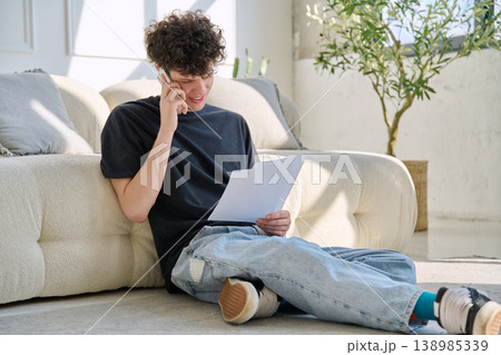 Young handsome guy, 20s university student talking on cell phone with paper documents Young handsome guy, 20s university student talking on cell phone with paper documents 138985339