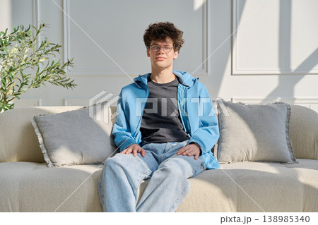 Portrait of handsome young man with curly hair sitting on sofa Portrait of handsome young man with curly hair sitting on sofa 138985340