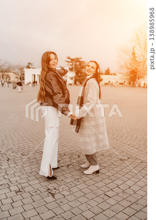 Friends walking plaza two young women hold hands and smile while walking through an urban square on a sunny autumn afternoon Friends walking plaza two young women hold hands and smile while walking through an urban square on a sunny autumn afternoon 138985968