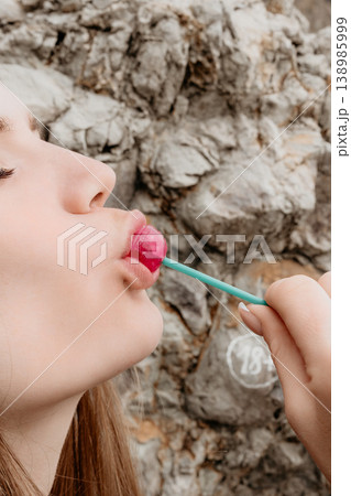 Lollipop woman portrait Woman enjoys tasting a pink candy sweet in front of a natural stone wall Lollipop woman portrait Woman enjoys tasting a pink candy sweet in front of a natural stone wall 138985999