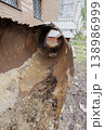 A rusted metal pipe is seen lying on the ground next to a brick building. The building shows signs of wear, with peeling paint and broken windows evident 138986999