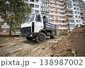 A truck stands beside a dirt pile near a residential building. Workers are preparing the site for construction in the afternoon light 138987002