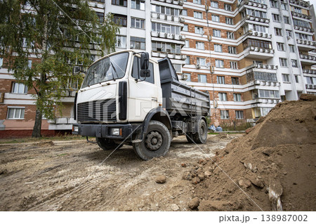 A truck stands beside a dirt pile near a residential building. Workers are preparing the site for construction in the afternoon light 138987002