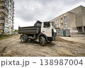A construction truck stands on a dirt surface near two buildings during cloudy weather. The truck is ready for work at the construction site 138987004