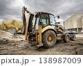 A backhoe is parked on a construction site while other machinery is visible. The sky is cloudy and the site shows signs of ongoing work 138987009