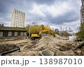 Heavy machinery is digging in the ground at a construction site near a tall building and old houses on a cloudy day in the city 138987010
