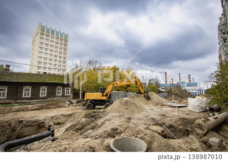 Heavy machinery is digging in the ground at a construction site near a tall building and old houses on a cloudy day in the city Heavy machinery is digging in the ground at a construction site near a tall building and old houses on a cloudy day in the city 138987010