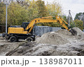 Heavy machinery works at a construction site, moving sand and dirt around while trees display autumn colors and power lines are visible in the background 138987011