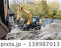 Loader machine works on dirt at a construction site in a neighborhood. Trees with yellow leaves surround the area on a clear afternoon 138987013