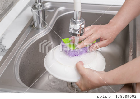 Washing a white plate in a kitchen sink using a sponge and soapy foam Washing a white plate in a kitchen sink using a sponge and soapy foam 138989602