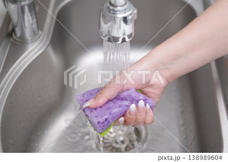 Hand rinsing a kitchen sponge under running water in a stainless steel sink Hand rinsing a kitchen sponge under running water in a stainless steel sink 138989604