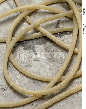 Tangled garden hose lies coiled on concrete outdoor surface forming abstract pattern background Tangled garden hose lies coiled on concrete outdoor surface forming abstract pattern background 138989682