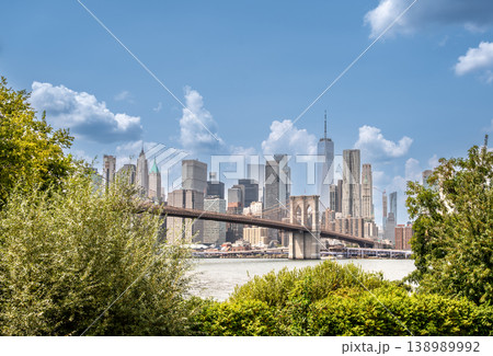 New york, usa august 15,2024. Iconic manhattan skyline with one world trade center, historic brooklyn bridge and east river framed by brooklyn greenery on a sunny day New york, usa august 15,2024. Iconic manhattan skyline with one world trade center, historic brooklyn bridge and east river framed by brooklyn greenery on a sunny day 138989992