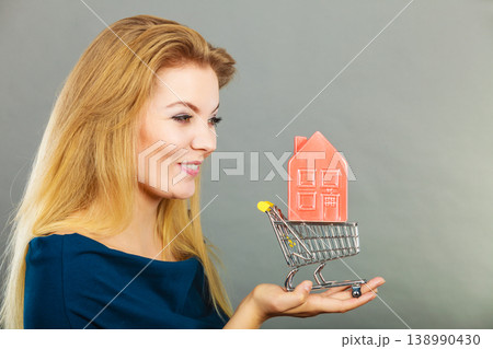 Woman holding shopping cart with house inside Woman holding shopping cart with house inside 138990430