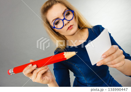 Serious woman holds big pencil note paper in hand Serious woman holds big pencil note paper in hand 138990447