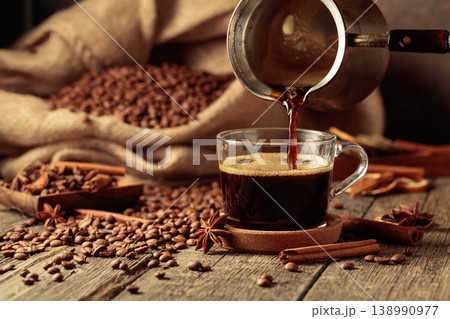 Black coffee is poured from a copper coffee pot into a glass cup. Black coffee is poured from a copper coffee pot into a glass cup. 138990977