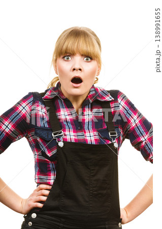 Surprised woman wearing dungarees and check shirt Surprised woman wearing dungarees and check shirt 138991655