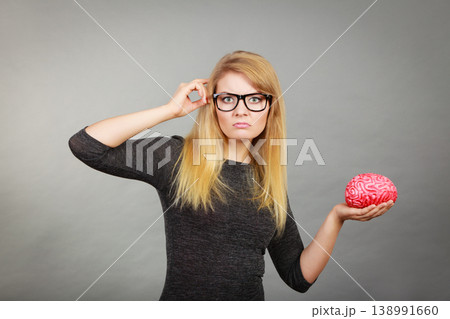 Woman in eyeglasses being confused holding brain 138991660