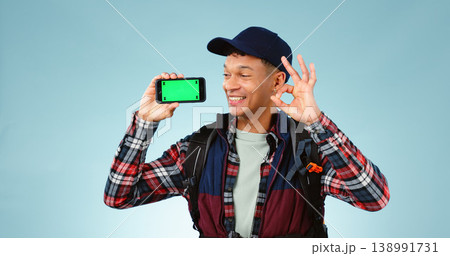 Hiking, green screen and man with a smartphone, ok sign and happiness on a blue studio background. Person, hiker and model with perfect symbol, agreement and cellphone with tracking markers and smile Hiking, green screen and man with a smartphone, ok sign and happiness on a blue studio background. Person, hiker and model with perfect symbol, agreement and cellphone with tracking markers and smile 138991731
