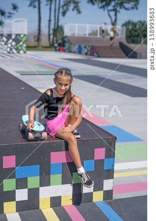 A happy athletic girl with a skateboard sits on the ramp of a skate park. Extreme sports lessons. A happy athletic girl with a skateboard sits on the ramp of a skate park. Extreme sports lessons. 138993683