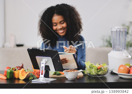 Young nutritionist showing bell peppers during an online video call consulting about healthy eating, sitting at home at a table with vegetables, laptop and measuring tape Young nutritionist showing bell peppers during an online video call consulting about healthy eating, sitting at home at a table with vegetables, laptop and measuring tape 138993842