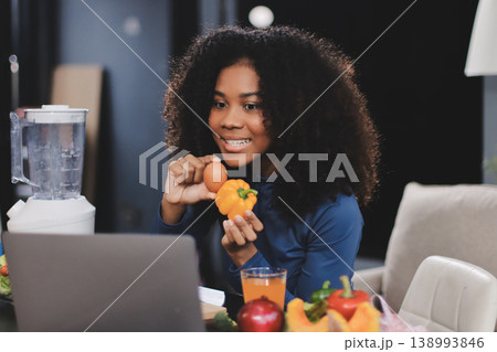 Young nutritionist showing bell peppers during an online video call consulting about healthy eating, sitting at home at a table with vegetables, laptop and measuring tape Young nutritionist showing bell peppers during an online video call consulting about healthy eating, sitting at home at a table with vegetables, laptop and measuring tape 138993846