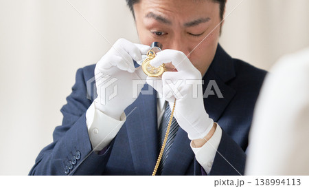 スーツと白手袋を着用した男性鑑定士がルーペを使って時計を鑑定する様子 138994113