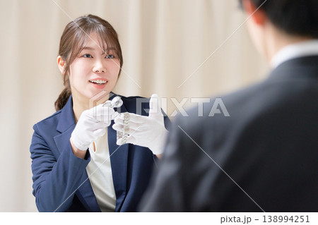 白手袋を着用したスタッフが腕時計を確認し顧客に説明する買取査定の様子 138994251