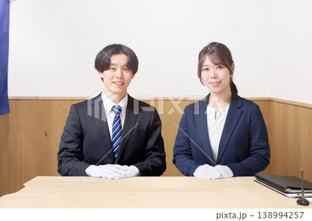 スーツ姿に白手袋を着用して接客カウンターに座る男女スタッフ 138994257