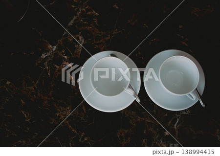 Two cups with spoon on marble table. Pair of white coffee cups with copy space. Hotel service. Morning hot drinks. Clean cutlery concept. Cozy lifestyle. White ceramic cups on plates. Two cups with spoon on marble table. Pair of white coffee cups with copy space. Hotel service. Morning hot drinks. Clean cutlery concept. Cozy lifestyle. White ceramic cups on plates. 138994415