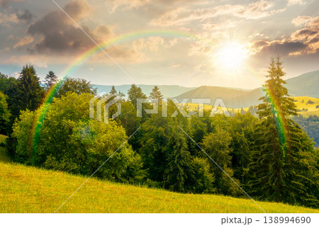 sunset over mountain hay field. alpine countryside summer landscape with green valley behind the woods on the grassy slope. cloudy sky. spectacular highland background under the rainbow 138994690