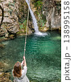 Close-up of a woman holding a bungee cord against the backdrop of a turquoise waterfall in a forest. 138995158