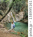Young Woman Standing Near Hidden Turquoise Waterfall in Lush Green Forest 138995161