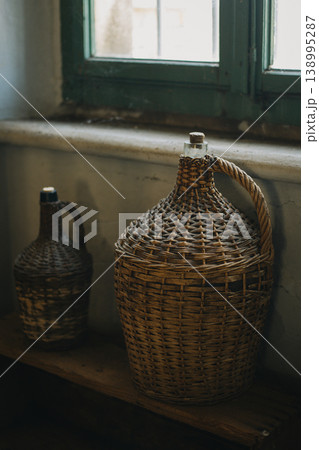 Vintage wicker wine bottles near the window. 138995287