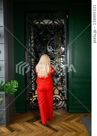 Woman dressed in red engages with ornate gate in luxurious setting 138995331
